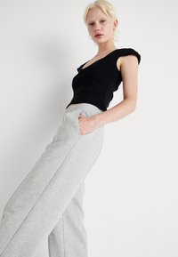Schwarzes, eng anliegendes T-Shirt mit kurzen Ärmeln, kombiniert mit hellgrauen, elastischen Sweatpants mit seitlichen Taschen und entspannter Passform.