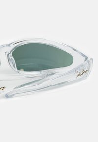 Occhiali da sole trasparenti con un design audace e angolare, dotati di lenti a tinta verde e una finitura lucida. Logo 'Ivy Sport' in oro sulla stecca.