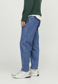 Jeans de mezclilla azul con un corte holgado, que presentan un diseño de pierna recta, detalles de costura y una textura desgastada. Combinados con zapatillas deportivas ligeras.