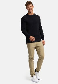 Zwarte textuursweater met een zigzagpatroon, gecombineerd met licht kaki broek en witte sneakers, die een ontspannen pasvorm en casual stijl laten zien.