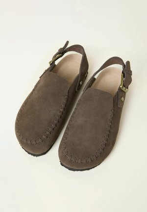 Brune ruskinds slip-on sko med syninger, slingback rem og messing spænde detaljer. Blød tekstur og rundet tåform.