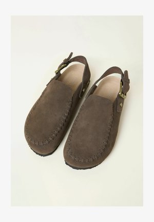 Ruskeat mokkaiset slip-on-kengät ommellulla kuvioinnilla, remmillä takaosassa ja messinkisillä solkikoristeilla. Pehmeä pinta ja pyöreä kärkimuoto.