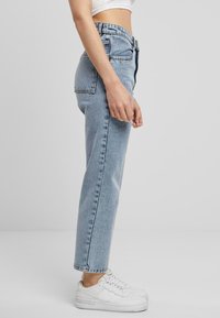 Vaqueros de mezclilla de mezclilla clara de cintura alta con un corte recto, con costuras visibles y dos bolsillos traseros, combinados con zapatillas blancas.