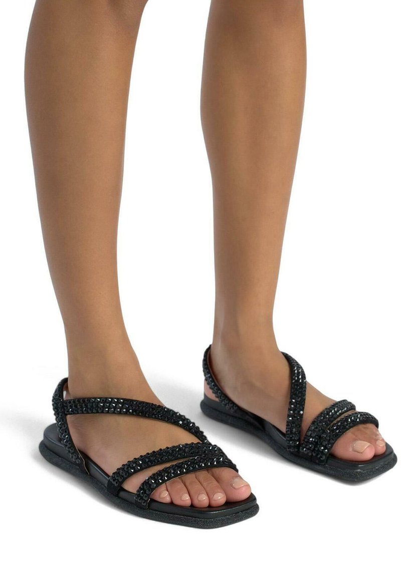 Zwarte platte sandalen hebben gekruiste banden versierd met rhinestones. De zool is glad en het ontwerp toont een open teen in een minimalistische stijl.