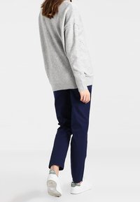 Grå stickad tröja med en lös passform, i kombination med mörkblå byxor och vita sneakers. Tröjan har ribbad fåll och sänkta axlar.