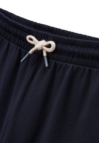 Pantalons de survêtement bleu marine avec taille élastique, dotés d'un cordon de serrage beige avec embouts. Tissu doux et texturé avec une légère élasticité.