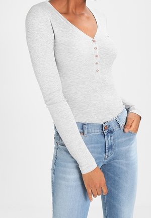 Grijze geribbelde longsleeve top met een V-hals en een vijfknopensluiting, gecombineerd met lichtgewassen denim jeans.