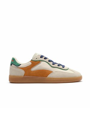 Zapatilla deportiva baja con paneles de ante beige, marrón y verde, cordones azul marino y suela de goma, mostrada desde el lado exterior sobre fondo blanco.