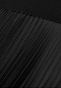 Détail d'une jupe plissée en tissu noir avec une ceinture lisse et des plis verticaux créant texture et profondeur.