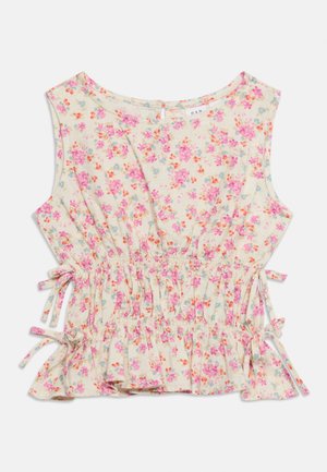 Blouse beige sans manches avec motif floral rose, orange et bleu, fronces à la taille et nœuds latéraux noués.