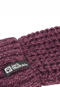 Un bandeau tricoté d'une riche couleur prune, présentant un motif texturé, en fil épais, et une étiquette noire avec un logo blanc.
