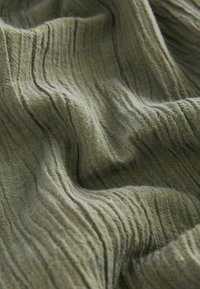 Textile with a textured, ripple pattern in olive green. The fabric appears soft, lightweight, and slightly sheer, with visible fibers.