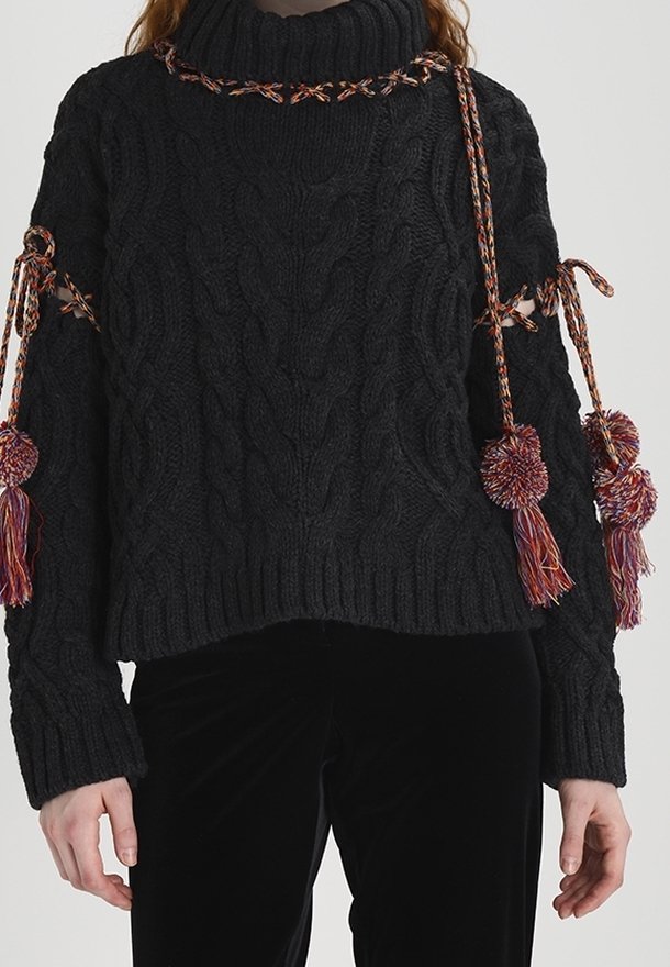 Maglione nero a maglia con colletto alto, caratterizzato da motivi a treccia, dettagli intrecciati e decorazioni a pompon sulle maniche.