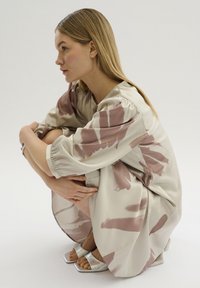 Ljust beige klänning med abstrakt rosa penseldragsmönster, lös passform, samlade ärmar och glänsande silversandaler. Mjuk tyg och avslappnad form.