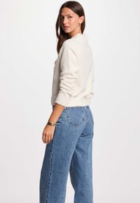 Krämfärgad stickad tröja med ribbade ärmslut, i kombination med hög midja blå denimjeans med bakfickor. Slät textur och avslappnad passform.