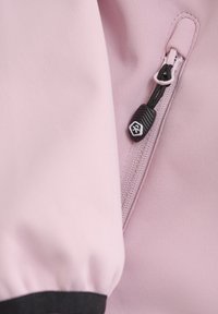 Un tessuto rosa con una texture liscia presenta un polsino nero, evidenziando una complessa linguetta della cerniera con un design contrastante a forma esagonale.