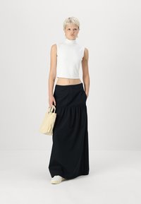 Hvit ermeløs turtleneck topp kombinert med et svart maxiskjørt med rynket midje, komplementert av en lys beige veske og hvite joggesko.