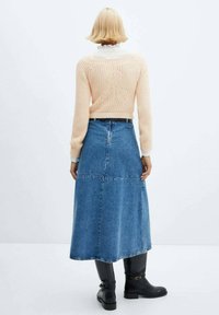 Pull pêche en tricot avec motif floral au dos, assorti à une jupe maxi en denim bleu et des bottes noires montant jusqu'aux genoux.