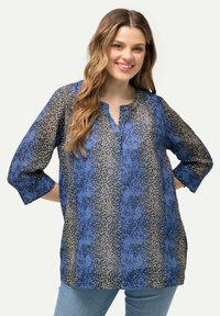 Blusa azzurra fluida con un motivo astratto mescolato in beige e blu navy, collo a bottoni e maniche a tre quarti.