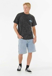 Camiseta de mineral negra con detalle de logo azul, combinada con pantalones cortos de denim claros y zapatillas negras, con un corte relajado y cuello redondo.
