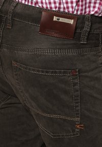 Donkergrijze denim broek met contrasterende oranje stiksels, een bruin leren merklabel op de achterkant en een traditionele vijfzakkenontwerp.