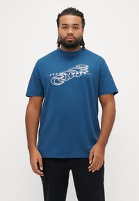 Blå bomuld T-shirt med rund halsudskæring, med et hvidt grafisk design og teksten "JACK & JONES 1990" centreret på fronten.