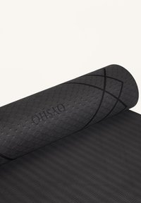 Černá yoga podložka s texturovaným povrchem s geometrickým vzorem a jemným logem. Částečně stočená, aby byly viditelné detaily designu.