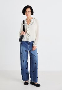 White blouse with black ruffles, paired with baggy blue denim jeans featuring black floral appliqués, and black platform shoes.