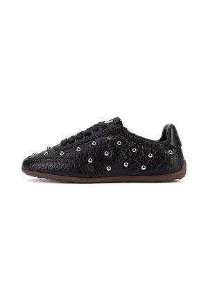 Zapatilla de cuero negro texturizado con cordones negros y pequeños remaches redondos plateados que decoran la parte superior, suela marrón.