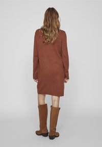Vestito in maglia marrone, maniche lunghe, vestibilità rilassata, polsini e orlo a coste. Abbinato a stivali alti in suede marrone con tacco a blocco.