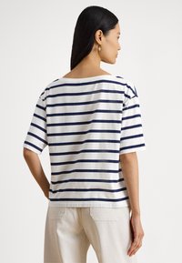 T-shirt às riscas em branco e azul-marinho, com mangas curtas, decote largo, corte solto e textura suave de algodão. Vista traseira mostrada.