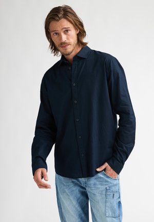 Marineblaue, langärmelige Hemdbluse aus weichem Stoff, mit klassischem Kragen und lockerer Passform, kombiniert mit hellblauen Cargohosen.