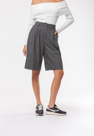 Shorts grigi a righe con vita alta e chiusura a bottoni, abbinati a un top bianco a spalla scoperta con effetto costina e sneaker nere.