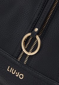 Borsa a mano in pelle nera con finitura testurizzata, accessori color oro, una cerniera prominente e un cursore rotondo con dettaglio logo.