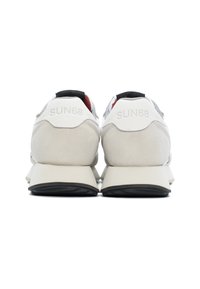 Zapatillas que presentan una parte superior blanca con acentos de ante gris, una etiqueta en el talón negra, un forro interior rojo y una suela gruesa blanca y negra con detalles de logo.
