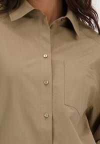 Lichtbruine button-up overhemd met een kraag, voorzien van een borstzak en een subtiele glans, gemaakt van zachte, gladde stof met een schone uitstraling.