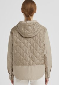 Beige gesteppte Jacke mit Kapuze, die eine glatte Oberfläche und ein strukturiertes Muster auf dem Rücken aufweist. Lange Ärmel mit Knopfdetails.