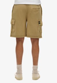 Pantalones cortos de cargo color caqui con doble bolsillo lateral, bolsillo trasero, dobladillo cosido y tejido de mezcla de algodón, que se llevan con zapatos y calcetines de color neutro.