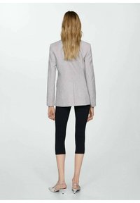 Lys grå blazer med en skræddersyet pasform og enkelt slid, parret med sorte cropped leggings og sølvfarvede strop-sandaler, set fra bagsiden.