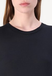 Crna pamučna majica s rebrastim okruglim izrezom. Glatka tekstura i prilagođen dizajn koji naglašava područje prsa. Nema vidljivih uzoraka ili akcenata.