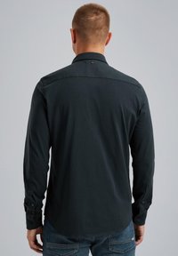 Tummanvihreä pitkähihainen paita, jossa on sileä pinta, napilliset hihansuut ja pistekaulus. Takana yoken lähellä pieni logo.