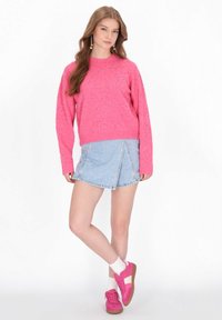 Rózsaszín kötött pulóver szemcsés részletekkel, világoskék farmer szoknyával párosítva. A modellen rózsaszín sportcipő van fehér részletekkel és fehér zoknikkal.
