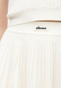 Εκλεκτικό κοντινό πλάνο στη μέση μιας λευκής φούστας από ριμπ πλεκτό ύφασμα με πιετέ ύφασμα και ραμμένη ετικέτα της μάρκας ellesse.