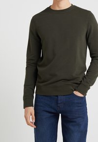 Felpa verde oliva con maniche lunghe, coltondo, polsini e orlo a costine. Abbinate a jeans blu scuro, con tessuto liscio e design casual.
