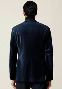 Námorníckomodrá zamatová blejzer s priliehavým strihom, pregĺbovaným golierom, dvomi bočnými vreckami a hladkou textúrou.