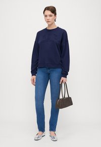 Sudadera azul marino con el logotipo "GAP" en relieve, combinada con jeans de corte ajustado. Zapatos planos plateados y un pequeño bolso marrón completan el conjunto.