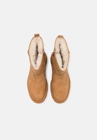 Paire de bottines en daim beige avec doublure en fausse fourrure crème visible et fermetures éclair latérales, vues de dessus.