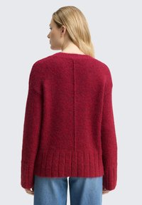 Czerwony sweter dziany o fakturowanym wykończeniu, z prążkowanym dołem, szerokimi rękawami i detalem z przeszyciem na środku pleców. Luźny fason.