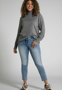 Grå rullekrage med långa ärmar, kombinerad med ljusblå, avklippta jeans. Modellen bär svarta och vita sneakers.