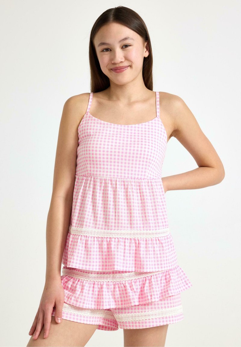 Różowa bluzka w kratkę w stylu gingham, z ramiączkami spaghetti, falbanami i białymi koronkowymi akcentami, w komplecie z dopasowanymi szortami o podobnych detalach.